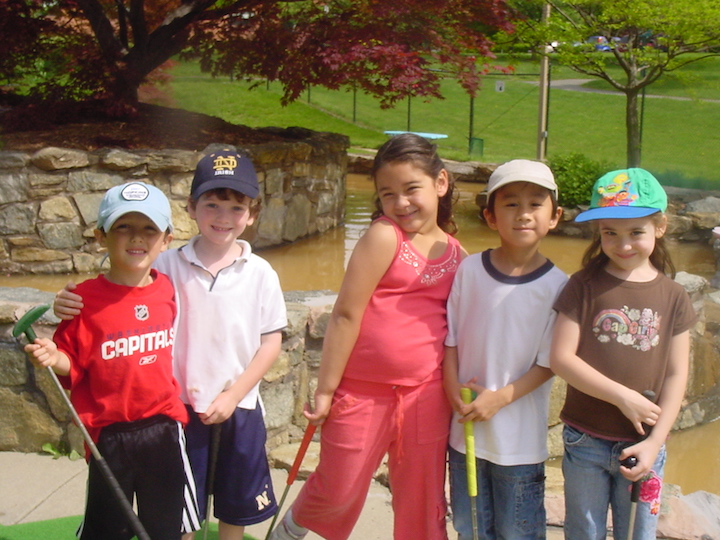Five preschoolers holding putt-putt golf clubs at mini-golf