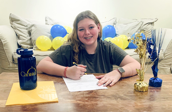 Student signing paperwork with balloons in background 