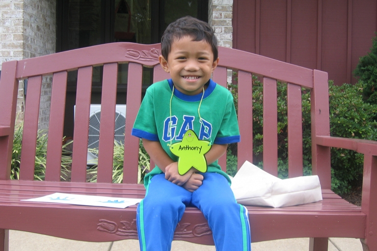 Student smiling, sitting on bench, on first day of preschool